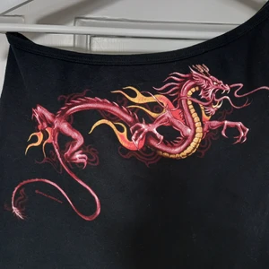 off shoulder topp med tryck - en off shoulder crop top i svart trikåtyg med tryckt drake där fram. jättefint skick, knappt använd och trycket är intakt. passar strl s/m. jag möts upp i Malmö, annars betalar köparen en mindre summa för frakt. DMa för frågor/detaljer/bilder osv. 🐉