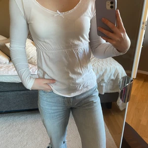 Vit långärmad t-shirt/tröja från Hickap - Tröjan är i storlek XS och kommer från Hickap. Den har en liten rosett fram och är insydd under brösten. Sparsamt använd och i fint skick. Säljs för 50 kr + frakt, som köparen står för. Betalning sker via Swish , hör av dig vid intresse🤍