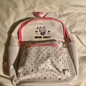 Hello kitty ryggsäck  - Söt vit liten hello Kitty ryggsäck. Ryggsäcken har rosa detaljer, hjärtan på dragkedjorna, små öron på toppen, och musik noter på fickan. Den har en inne ficka och två fickor på sidorna. Väskan är liten men inte för barn. Jag har massor med flera bilder så är du intresserad är det bara att fråga! Väskan är aldrig använd, jag säljer den just för den anledningen. Man kan få plats med A5 i den 🥰 