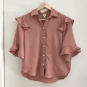 Rosa blus med pärlknappar - Superfin blus i dusty pink med volanger. Köpt på River Island men bara använd ett par gånger så den är i princip nyskick💕