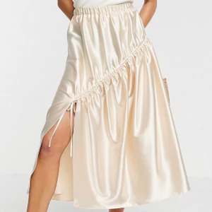 Maxi kjol  - Svin söt kjol från Asos i satin material. Längden slutar vid vaden och har en väldigt fin slits och rysch som man kan dra till om man vill. Champagnefärgad i strl 38. Köpt för över 400kr säljs för 150 ❤️