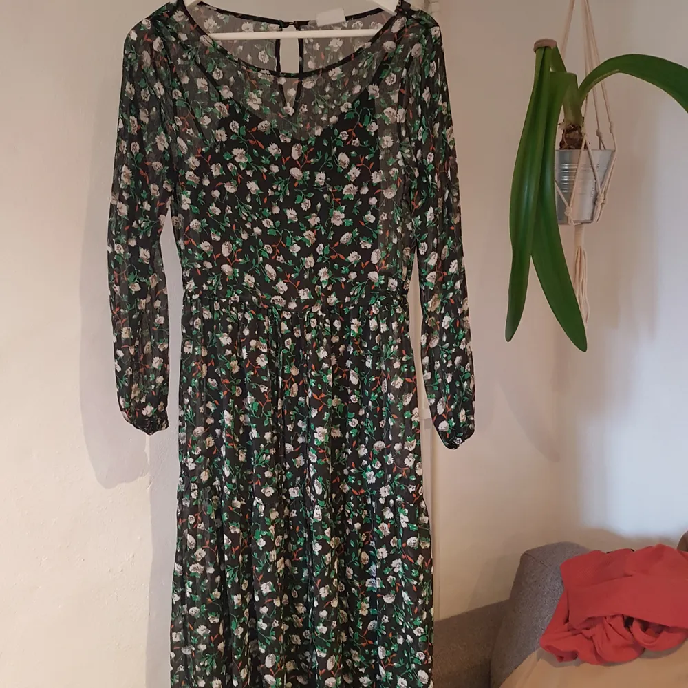 Black see through dress with green, white and orange flowers. The dress has a drawstring at the waist and a black slipdress attatched as a base layer. It's a little long on me (I'm 158cm) that's why I'm selling. . Klänningar.
