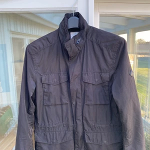 J.Lindeberg övergångsjacka - Hej! Jag säljer nu min J.Lindeberg jacka då den inte kommit till användning.   Det är en övergångsjacka som funkar lika bra på våren likasom på hösten. Jackan är gjord av ett vattenfrånstötande material vilket gör att den är lämplig även på regniga dagar. Men missförstå mig inte - den är inte Gore-tex:) I nacken finns det en luva som smidigt kan tas fram samt stuvas in igen.   Jackan är använd vid ett fåtal tillfällen & är därmed i princip i nyskick. Nypris på jackan var ca 2900:- men då den bar