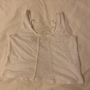 Vit topp med spetsdetaljer - En vit magtröja med spetsdetaljer i ett lite genomskinligt material. Köpt i Peru för några år sedan och använd ett fåtal gånger, nu för liten för mig. (50kr inkl. frakt)