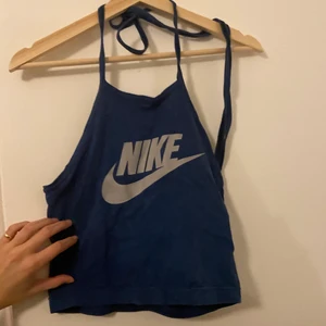 Nike halternecktopp - En marin/ mörkblå halterneck topp med Nike tryck i silver. Knytning i nacken. Lite cropped vid magen. Inga fläckar eller hål. Skriv vid funderingar.
