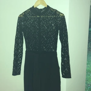 Jumpsuit - Snygg jumpsuit med ovandel i vacker svart spets och kostymliknande nederdel. Fickor och motveck i sidorna.