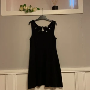 Svart klänning med fina detaljer strl xs - Använd fåtal gånger i väldigt fint skick. Strassdetaljer runt urringningen som föreställer blommor (kolla sista bild). Knapp i ryggen. Tjockare/stadigare tyg. Söm i midjan och mot brösten för att framhäva fina former. Strl xs.