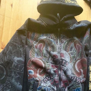 Zip Luvtröja Ed Hardy (?) y2k hoodie - Helt sjuk hoodie med feta tryck, guld embroidery osv. Klassiska EdH Detaljerna  o robusta tyget ger tröjan en riktig y2k vibe. Otroligt mysig o snygg, bra kvalitet. Gjord av ett bra tjockt tyg. Har perfekt passform/fit osv.                                                                              (Ej så insatt så är ej säker om det är riktig ed Hardy eller insp, det jag vet är att den är jävligt tung, älskar den😆) långt ifrån känslan av en billig hoodie.  Kvalitet: 10/10 skick 9/10