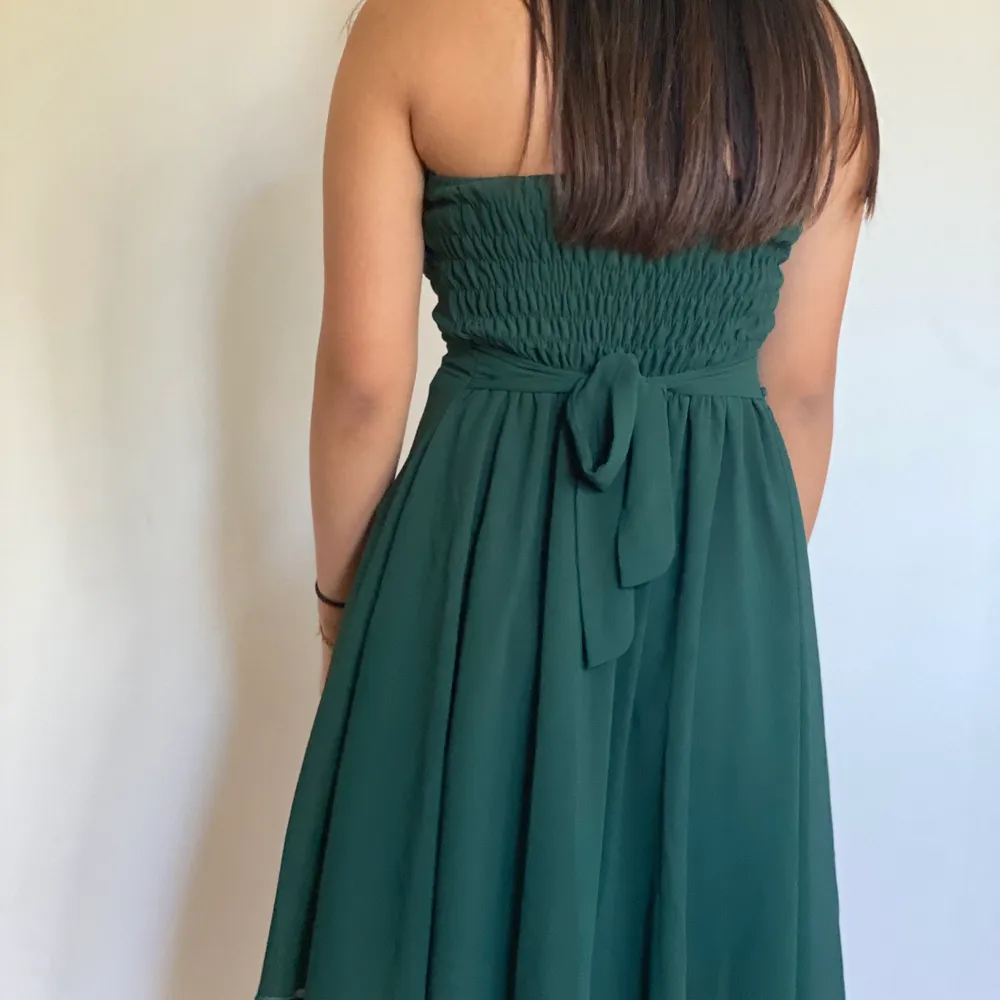 En kort of shoulder klänning i en mörkgrön färg. Runt midjan finns som ett bälte med ’blommor’ på. Använd mycket men i gott skick. Klänningar.