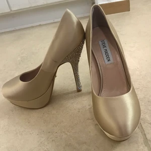 Högklackar från Steve Madden - Säljer dessa fina klackar från kända märket Steve Madden som är i beige färg med silver stenar på klacken. Storlek 36, säljer de för endast 100 kr.