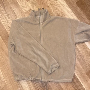 Fleecetröja - Mysig fleecetröja med dragkedja och dragsko vid midjan. Beige storlek XS. 