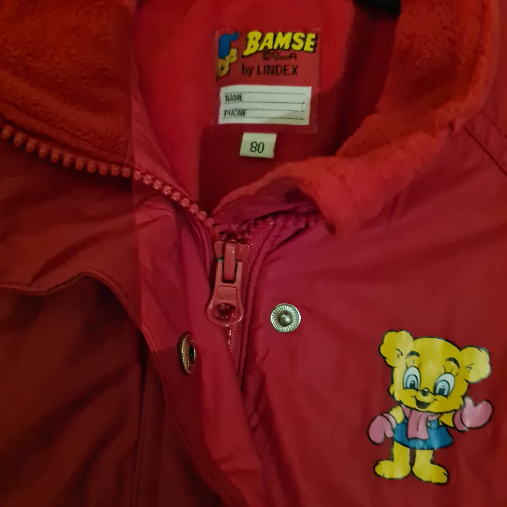 Röd Bamse jacka för en liten tjej. Storlek 80. Finns både dragkedja och knäppning.  På baksidan av ena ärmen finns en vit 