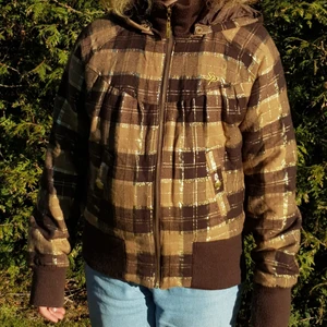 Rutig brun jacka - Detta är en jätteskön brun jacka med guldfärgade detaljer. Säljer då det inte riktigt är min smak. Luvan går att ta av (sitter fast med knappar) . Fickorna är riktiga och går att stänga med knapp. Vid frågor eller om ni vill ha fler bilder,kontakta:)