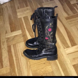 Svarta läderkängor storlek 35 - Svarta läderkängor/boots med broderade blommor, hel snörning och hel dragkedja från Bon’aparte. Storlek 35. Lite använda men i fint skick.