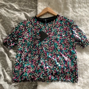 Paljett fest t-shirt - Detta är en T-shirt som är kladd i paljetter. Den är oanvänd, prislapp finns kvar. Den är ganska tunn i materialet.