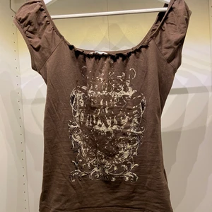 Brun topp med coolt tryck! - As fin topp (t shirt men går ner där bak) med typ y2k tryck haha, storlek S men passar nog xs också . Fraktas för 48kr/66 spårbart 😄