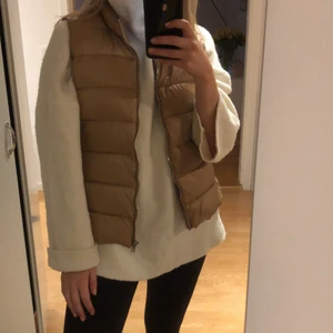 Mango väst - Väst i 100% polyamide. Använd ett fåtal gånger, inget att anmärka på i skicket. Färgen är beige/guld, bilderna gör den rättvisa. Fickor med dragkedja. Strl: L (men passar fint på en S/M). Färg