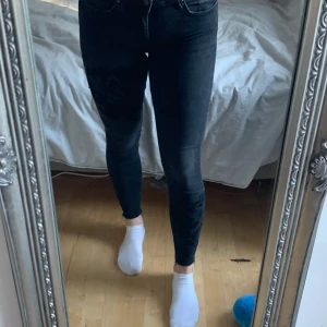 Svart jeans med ingraverade blommor  - Svarta jeans med låg midja, har stretch i sig. Ingraverade blommor i svart tråd