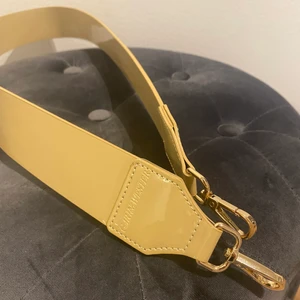 Väskband, beige  - Väskband i färgen beige, från Carin Wester. Guldiga detaljer. Använd några gånger. Frakt tillkommer! 