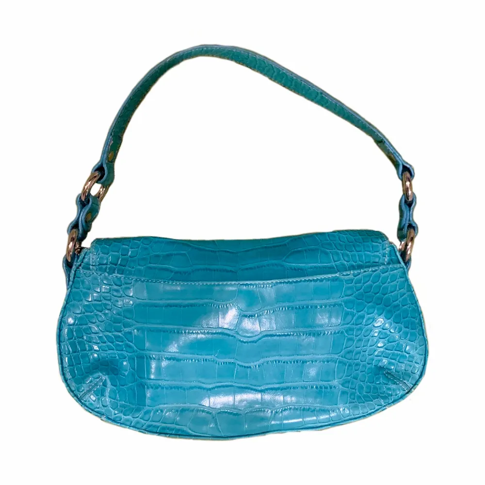 Fräck ljusblå väska med krokodilmönster och ett spänne på famsidan. Köpt på Humana, därav lite använd men inga tydliga defekter. . Väskor.