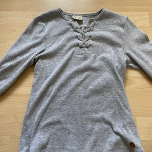 Grå tröja från kaphal med fläta vid kragen 158-164 - En grå ribbad tröja med en fläta högst upp vid kragen. Fint skick! Säljes för att jag inte kommer använde den mer. !!köparen står för frakten!! Tvättas innan den skickas