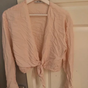 Ljusrosa blus med knytning - Gullig blus med knytning i fram och små volanger längst ner vid ärmarna. Aldrig använd. Storlek L. Väldigt skrynklig på bilden men kan stryka den och skicka fler bilder om det önskas!