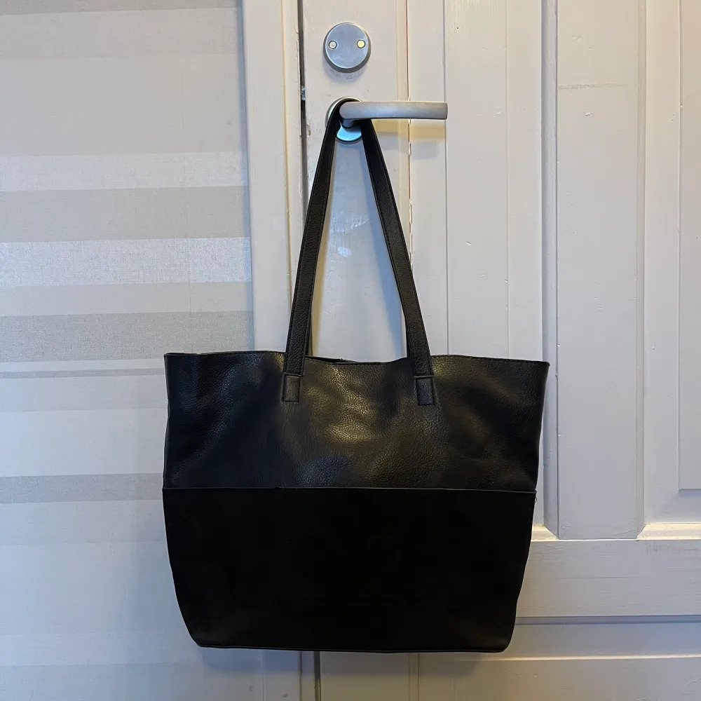En svart rymlig väska som är i fakeskinn & fakemocka material. Den är köpt på Åhlens för några år sedan. Sparsamt använd och i bra skick!. Väskor.