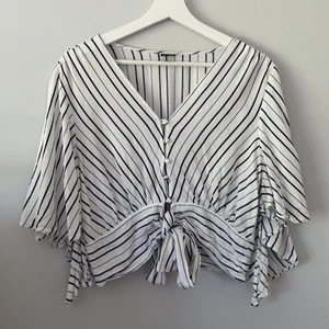 Gina tricot blus  - En randig blus från Gina tricot i storlek 42 (mer som 40). Den har knappar i mitten och en rosett som knyts i midjan. Ärmarna är ”fladdriga” och går ner till armvecket ungefär. Använd ca 2 gånger och i bra skick! Köparen står för frakt och returneras ej💙