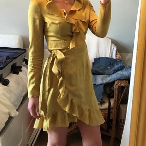 Klänning från Boohoo - Fin klänning i gul/grön färg från ”Boohoo”. Aldrig använd, i bra skick! Anpassbar omlottklänning med band i midjan som går att justera 🌼 såg nu att en söm vid byst har gått upp, dock lätt fixat.