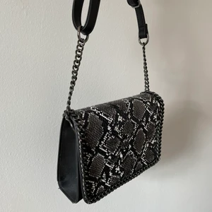 Väska - Fin väska med ormskinnsmönster på framsidan. Innerficka och dragkedja. Går att justera längden på axelbandet. Frakt ingår inte!