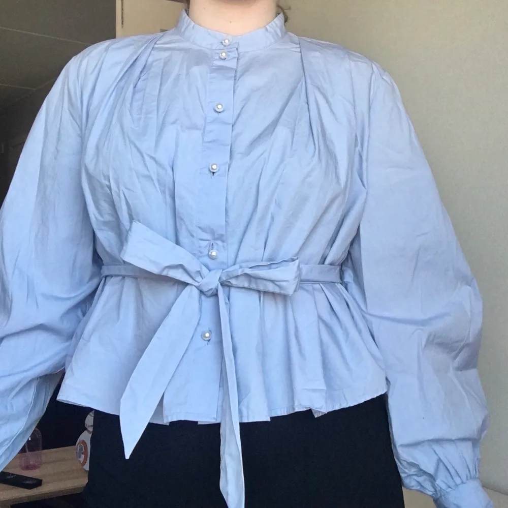 European size 44 with arm length from shoulder down 63cm, from neck down 49cm. Only tried on twice, condition good. The fabric is 100% cotton and with a light blue colour. Buttons are white pearls along the front and on the arms. From the back (look at detail picture) two waistbands can be tied like a ribbon at the front! . Blusar.