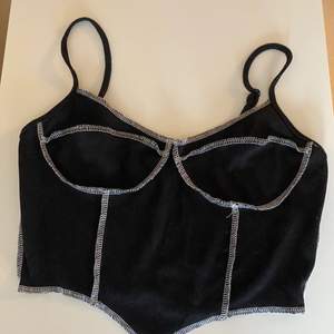 Simpel svart linne med vita sömmar. Triangelshape på framsidan ger illusion till en smalare waist. Crop top såklart färgerna på toppen passar typ till allt🤍