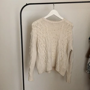  stickad tröja med pärldetaljer - Gräddvit stickad tröja med pärldetaljer från NA-KD. Använd enstaka gånger med i god skick. Pärlorna sitter kvar efter tvättning 