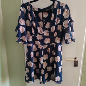 Otrolig shortsdress från TOPSHOP med volanger - V-ringad shortsdress från Topshop. Köpt i London, använd en gång. Volang på ärmarna, jättefint fall