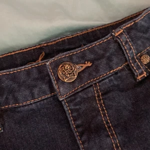 Mörk blå Basic jeans -  mörk blåa men en rosen knapp och detaljer på bak fickorna