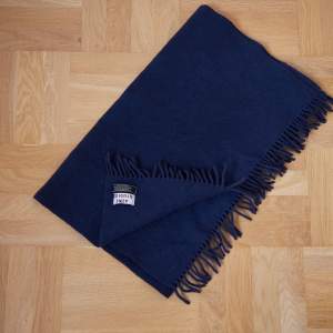 Stor mörkblå halsduk med fransar i lammull. I använt skick men utan defekter.