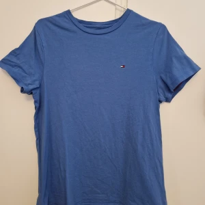 Tommy Hilfiger T-shirt blå - Köptes i USA och är i amerikansk storlek xs, men sitter som en S. Ganska använd, men enda riktiga tecknet på slitage är att texten i nacken börjar gå bort. Buda på!