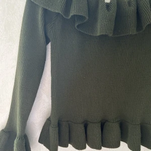 Off shoulder topp - En grön stickad off shoulder topp med volanger på armar och längstupp. Kortare modell. Använd några gånger. Passar en M-L