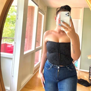 Korsett med blommor  - En ordentlig korsett-topp med ribbingar med svarta blommor och hakknäppning. Korsetten är stretchig och kan passa runt M-XL.