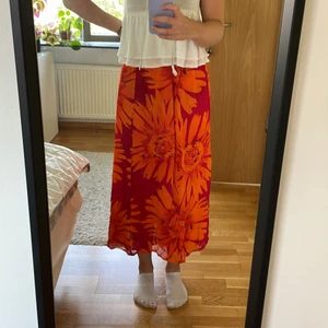 Oanvänd långkjol - Helt oanvänd långkjol (lapp kvar, se sista bild). Röd/orange med blommor på. Saknar storlek men har resårband så passar nog XS-M (jag har storlek S).