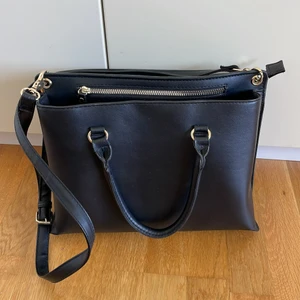 Svart handväska - Ganska stor (ca 30x20x10 cm) handväska i fakeläder med gulddetaljer. Två stora fack (ett med dragkedja och ett med knapp) + 2 mindre fack med dragkedja. Säljes pga aldrig använd.