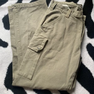 Cargo byxor - Beige/gröna cargo byxor som är väldigt baggy. Jag är ungefär 170 för referens. Sänkt pris pga. lösa knappar och igensytt hål.