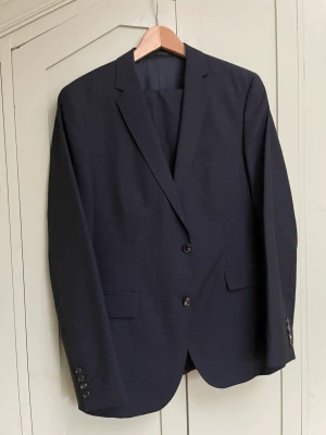 Boss kostym 50 - Lite använd ullkostym från Hugo Boss i midnattsblått. Helfodrad kavaj med framfickor med lock. Modell 183cm 82kg