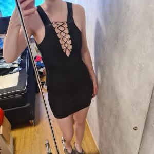 Svart miniklänning med V-ringning - Helt oanvänd miniklänning. Den har en V-ringning med snörning genom ringar som går till midjan.  Jag är 176cm lång