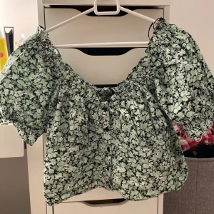 Blommig topp - En topp från ginatricot i strl 42. Ljusgrön blommig, svart och vit använd ett fåtal gånger. Svarta knappar och resår i ärmarna. För stor för mig så säljer. 60kr+frakt
