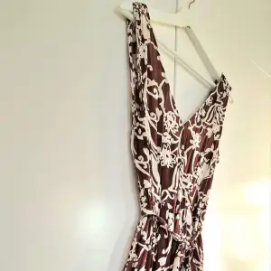 Storlek S Lång klänning i omlottmodell upptill med brunt mönster på ljus botten i viscos. Veckad i midjan med smalt knytband.  Pris 250 kr 