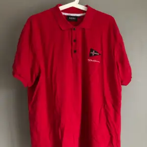 En röd pikétröja/kortärmad skjorta. Passar en large om man gillar lite oversized. Märke: Dahlin