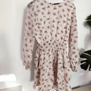 Blommig sommarklänning  - Superfin, tunn klänning med volanger. Passar alla mellan S-M/L. Beige/puderrosa färg med blommönster.