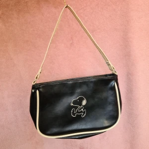 Snoopy/Snobben väska  - Super söt axelväska! Storlek på den är: 24cm x 16cm x 3,5cm! Axelbandet är kort, men tillräckligt lång att ha hängandes på axeln :)  Den har 3 väldigt små fläckar på insidan. Kan skicka fler bilder!