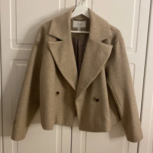 Kort kappa - Säljer denna superfina beiga kappan från Vila. Köpt förra våren men bara använd ett fåtal gånger så den är som ny! Köparen står för frakten